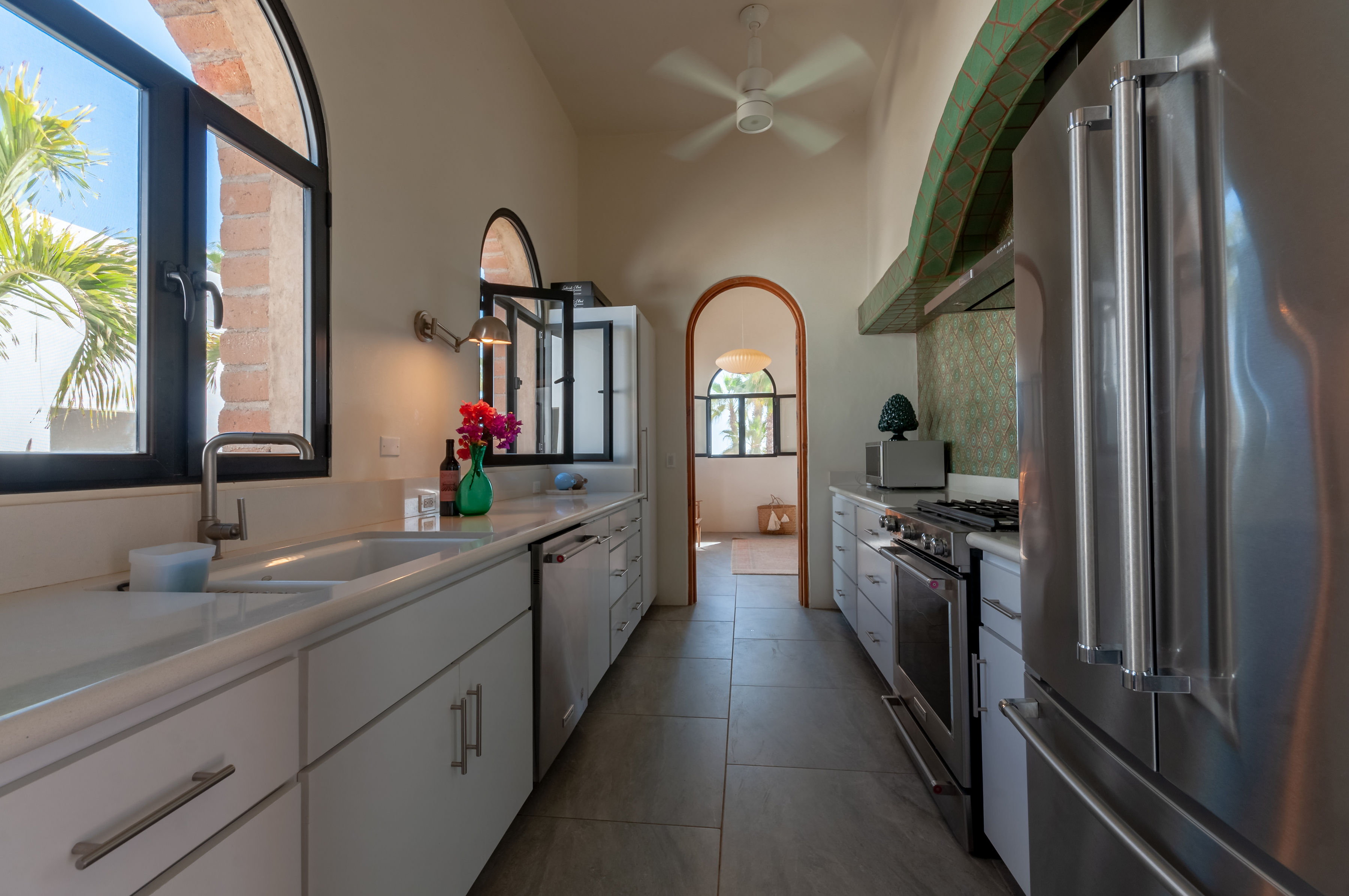 White galley kitchen in the Adobe House with green patterned tile, an arched brick window and stainless appliances