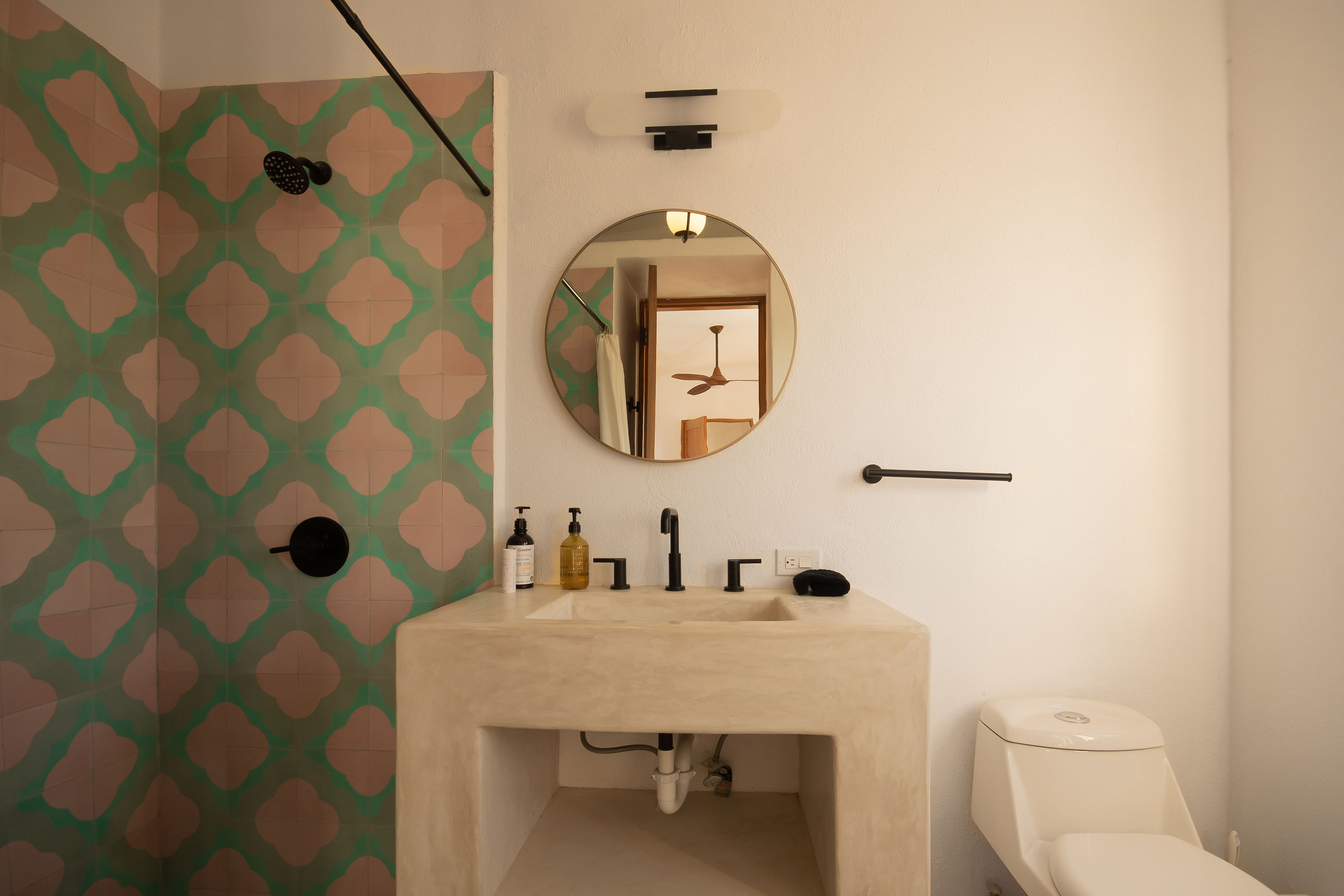 Casita bathroom with a green and pink patterned tile shower wall, a poured concrete vanity and a round mirror