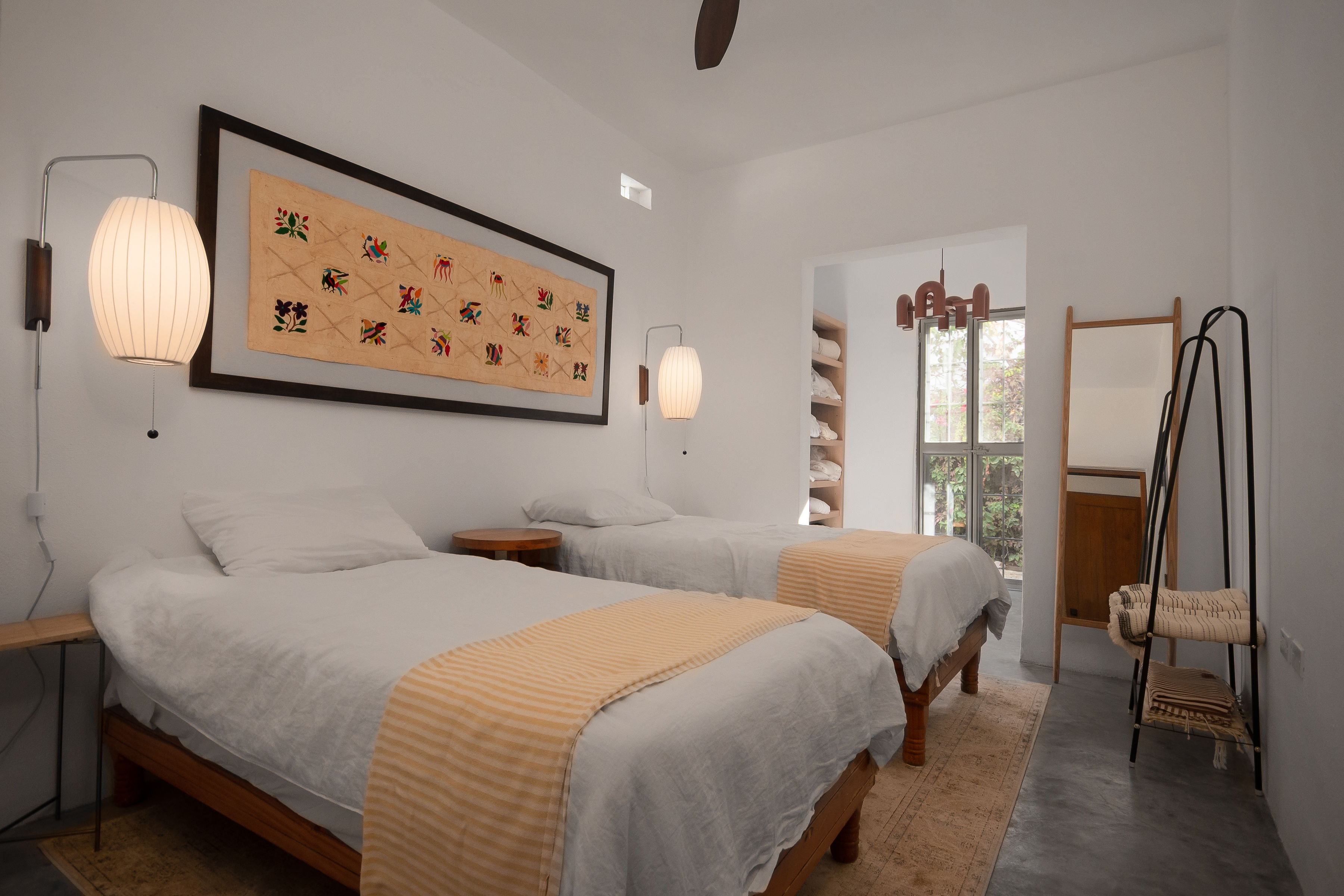 Downstairs bedroom in the casita with two twin beds, framed Otomí textile, paper lantern sconces and glass doors to the garden