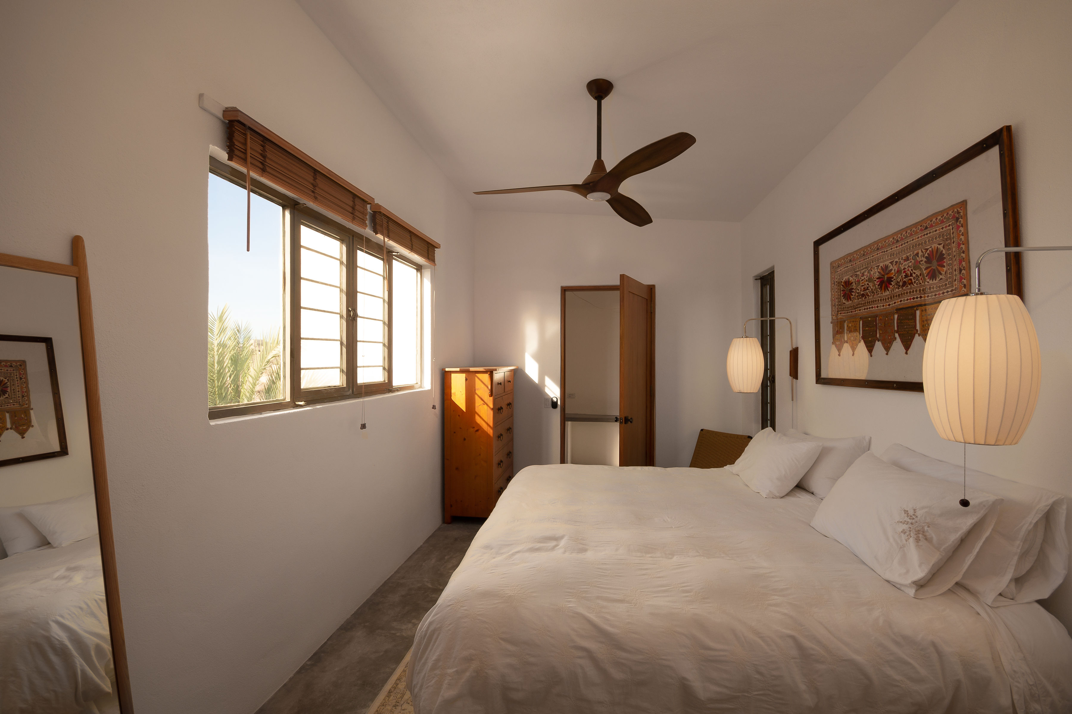 Upstairs bedroom in the casita with a king bed, ceiling fan and a window looking out over the palms