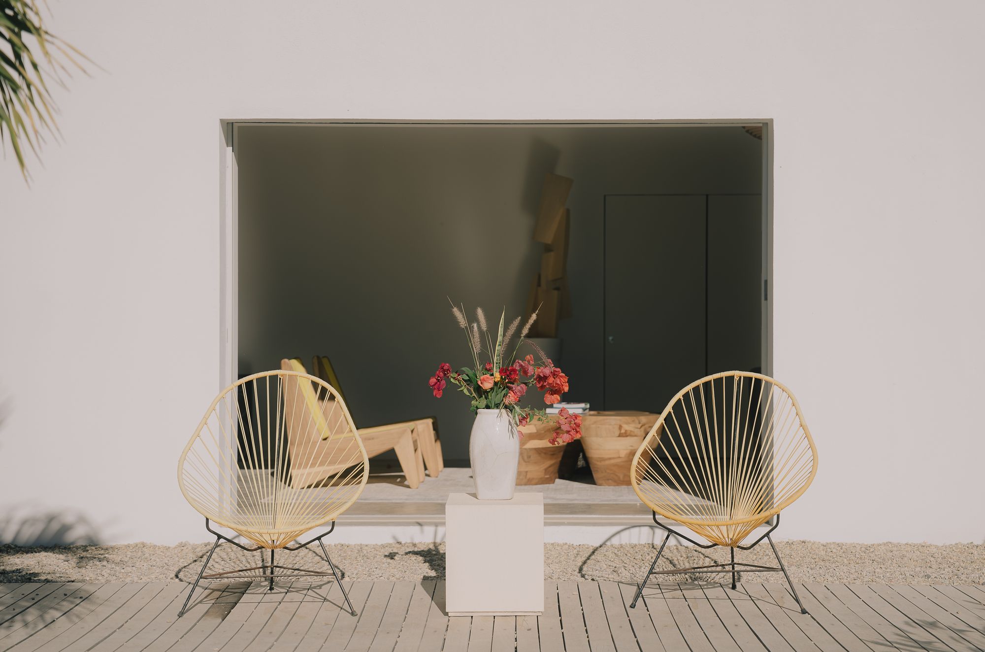 Two yellow Acapulco chairs flanking a plinth of flowers in front of an open doorway