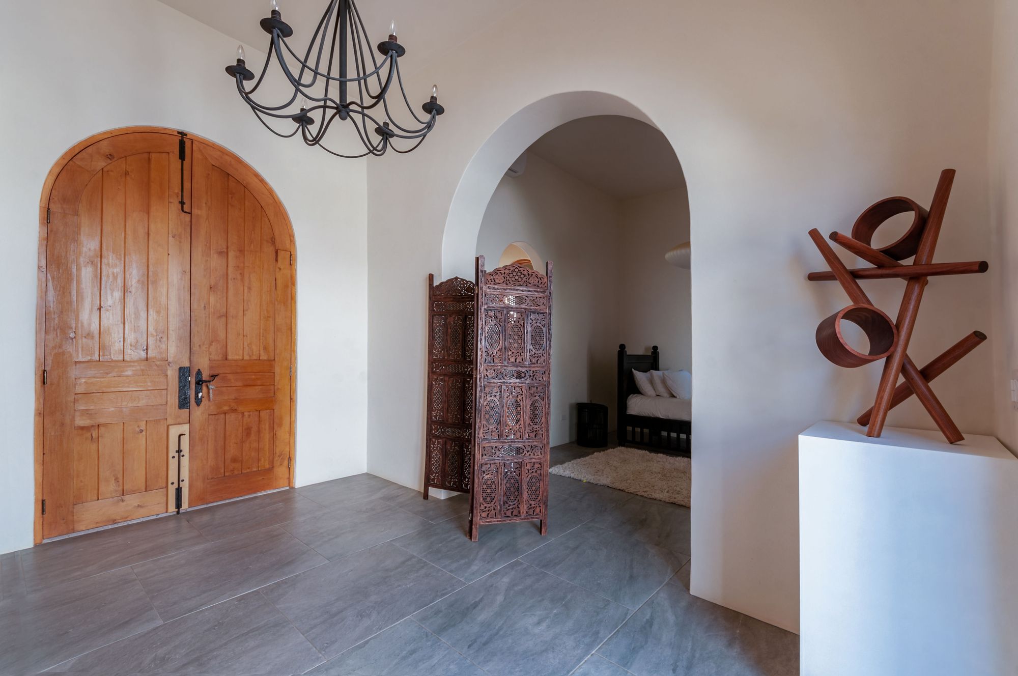 Entry hall with arched wooden doors, a carved screen and a timber sculpture on a plinth