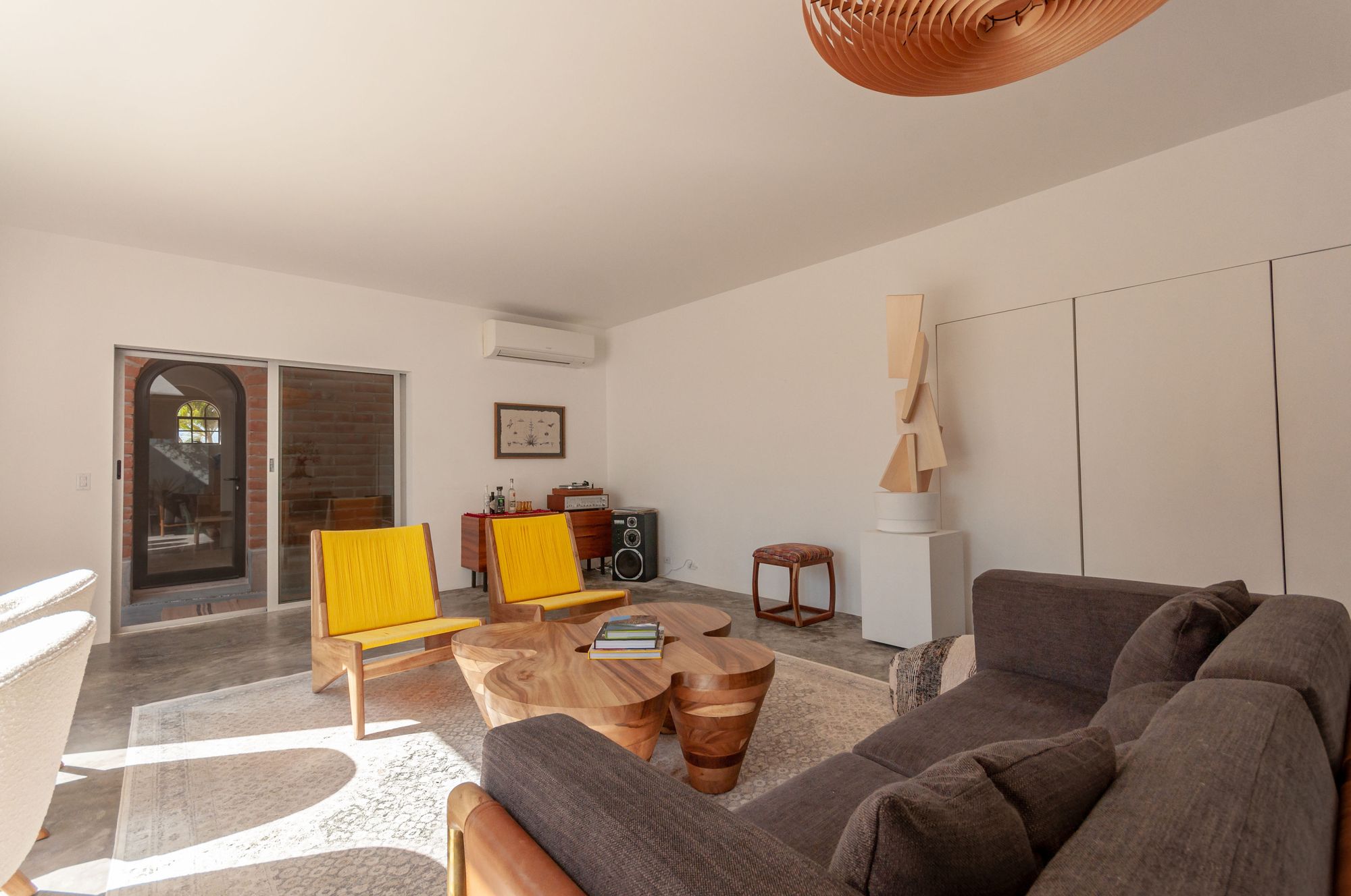 Living room with woven yellow chairs, a clover-shaped wooden table and a standing sculpture