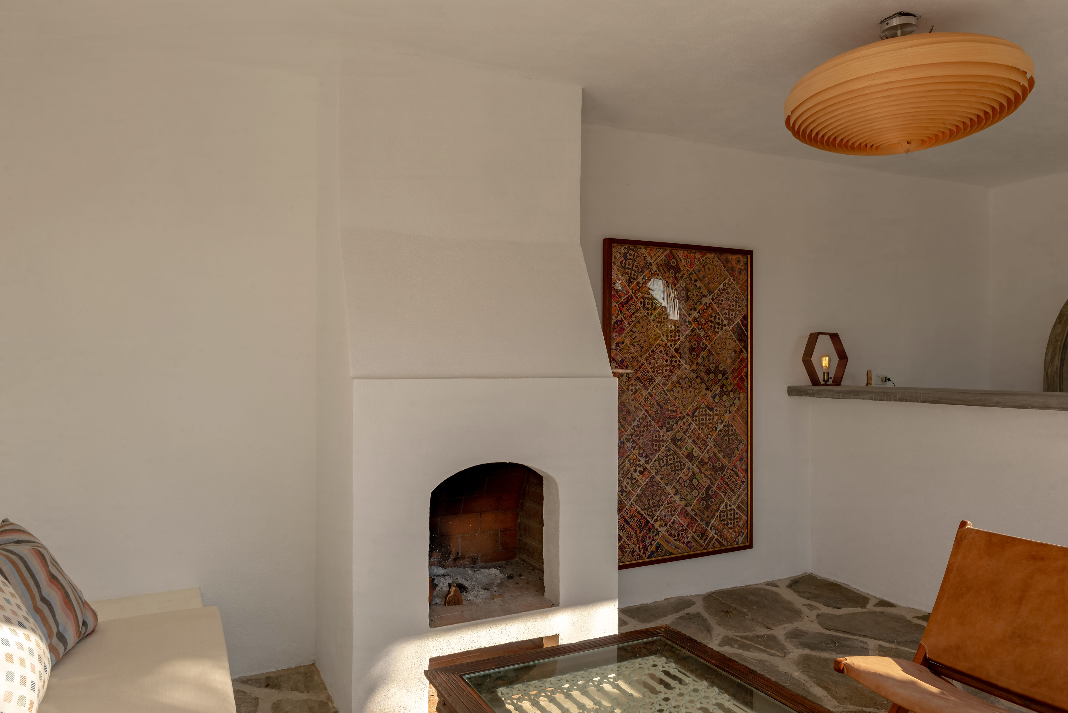 Inside the pool house cantina: a plastered corner fireplace, framed textile, flagstone floor and leather sling chair