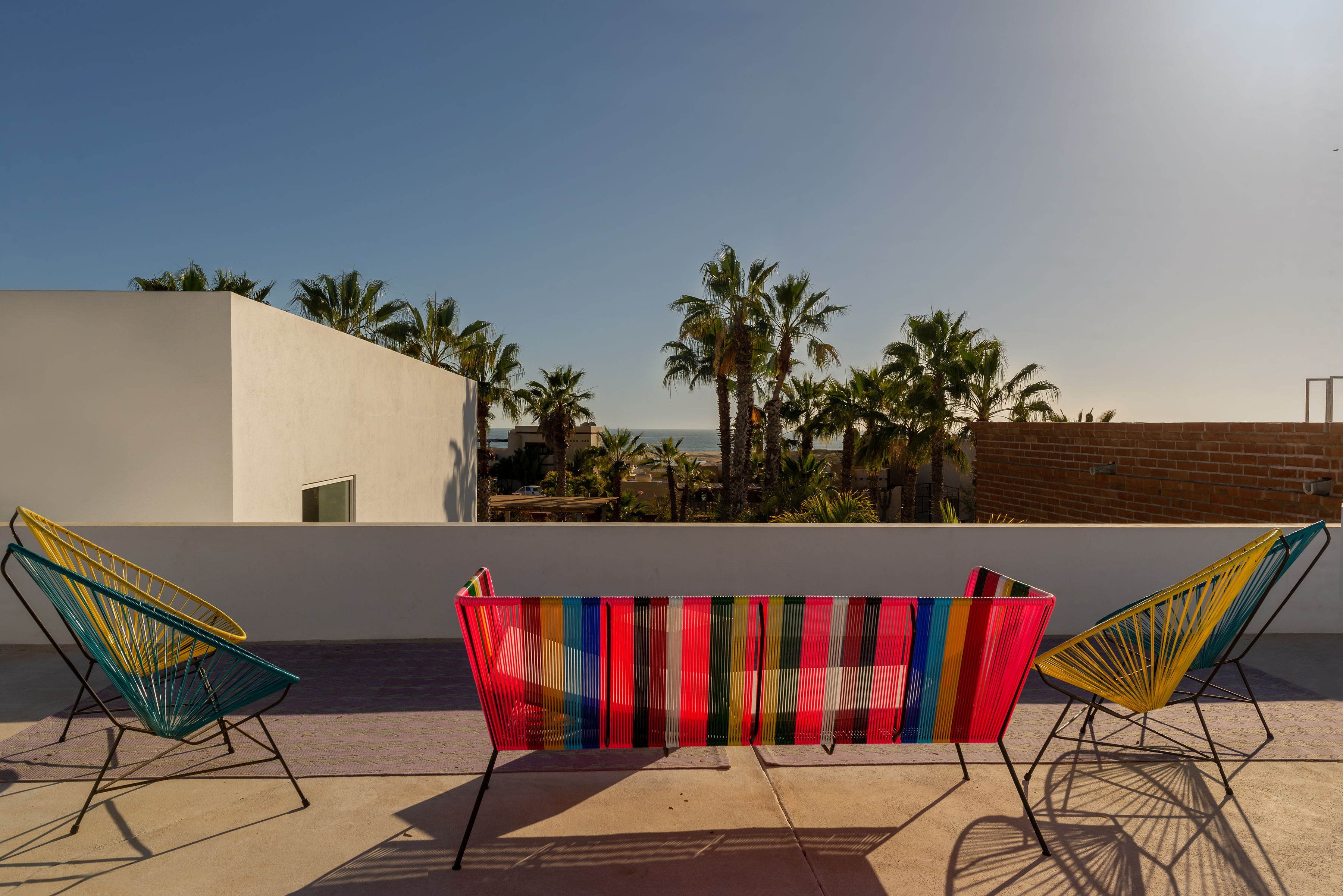 Rooftop terrace with woven Acapulco chairs and a striped bench facing the palms, with the Pacific visible beyond