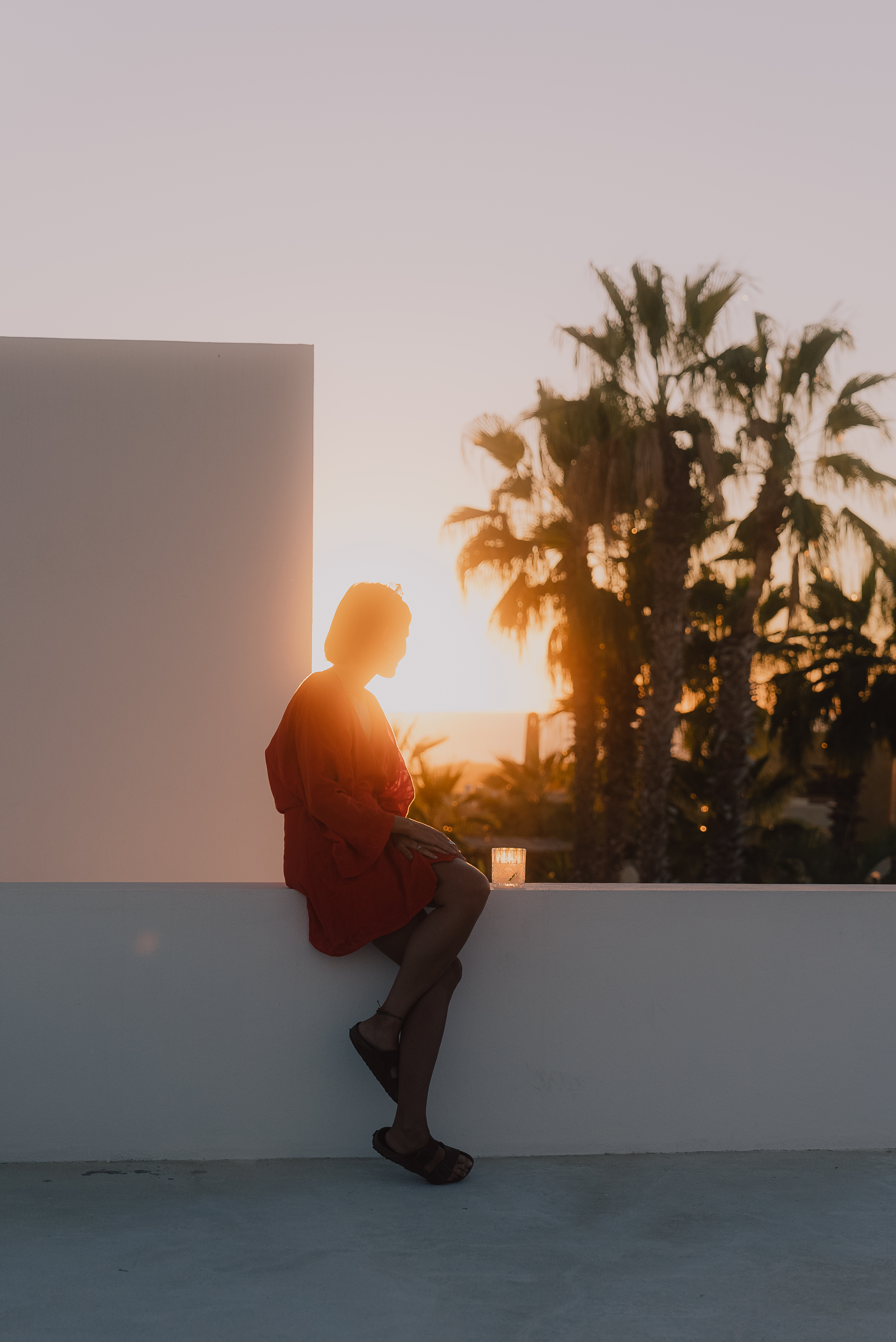 A guest watching sunset from the rooftop, silhouetted against the palms and the Pacific beyond