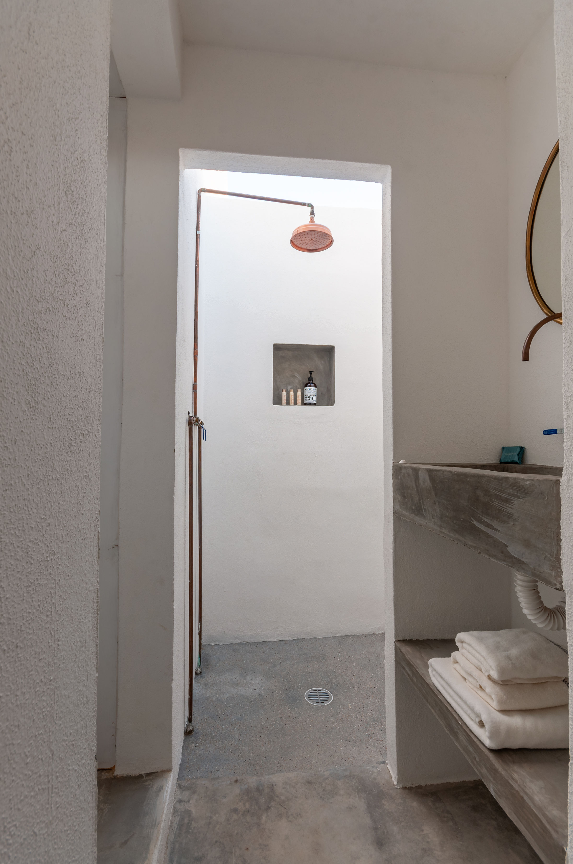 Outdoor shower off the studio bathroom, with a copper rain head, a plaster niche and a concrete basin with folded towels