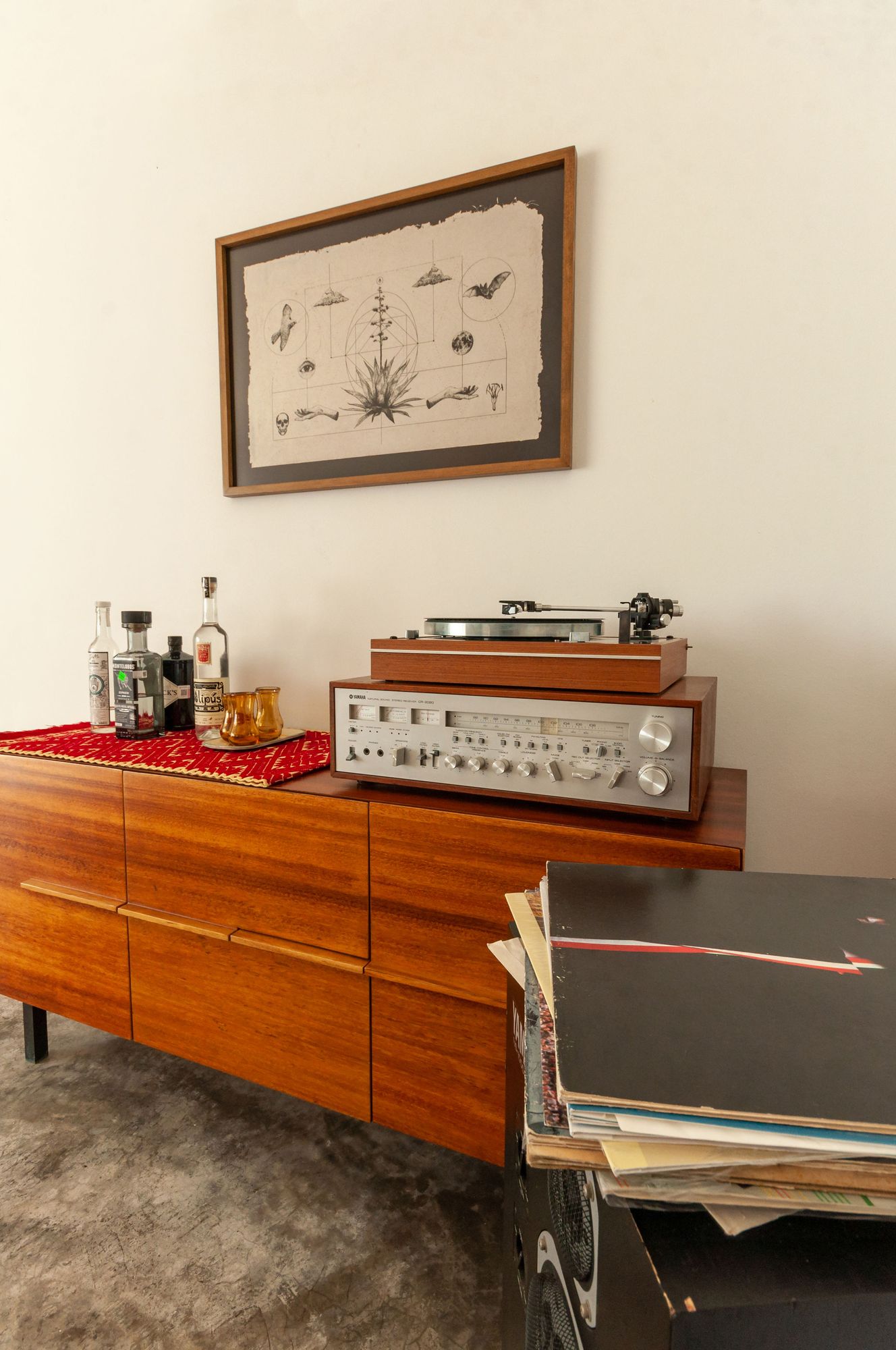 Turntable, receiver, records and mezcal on a wooden sideboard beneath a framed drawing